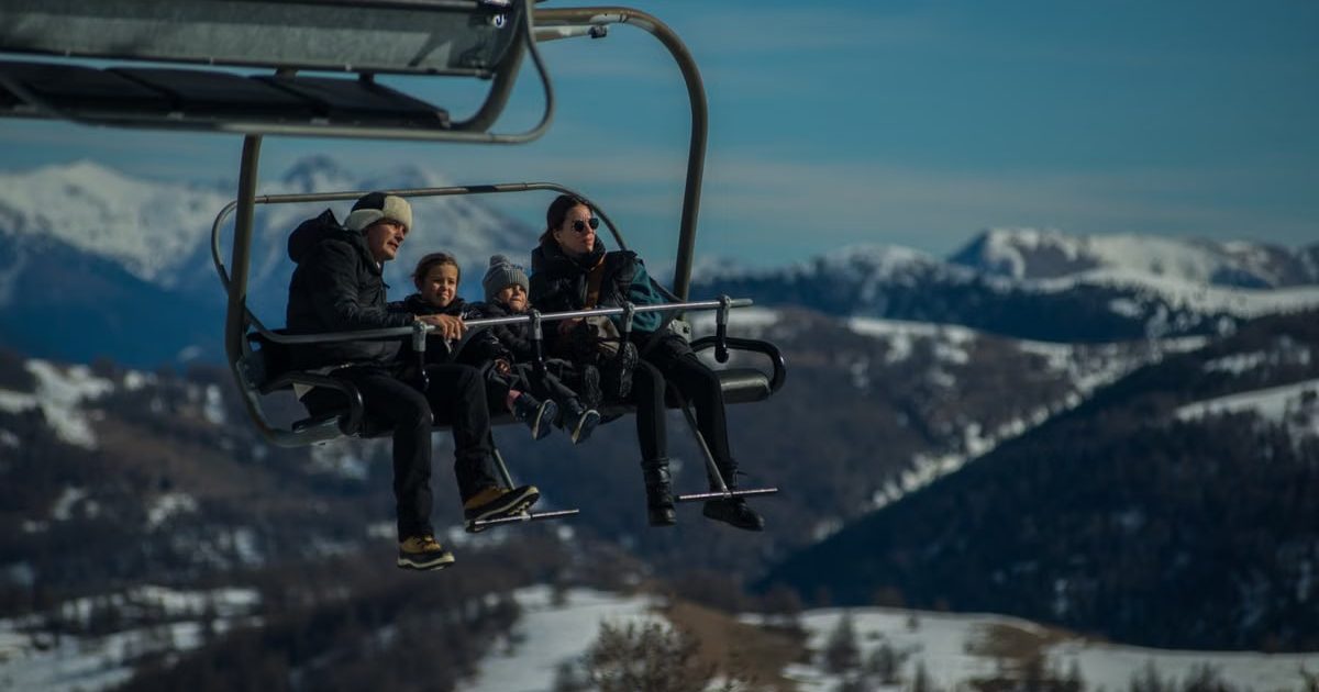 Family having fun on a ski lift with snow-covered mountains in the background during a sunny winter day.