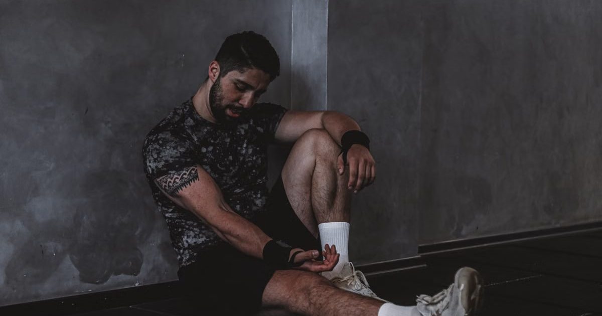A muscular man in a gym environment taking a moment of rest, reflecting in a dark moody setting.