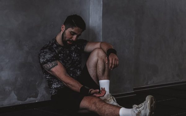 A muscular man in a gym environment taking a moment of rest, reflecting in a dark moody setting.